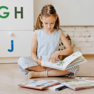 Young girl engrossed in reading books on the floor, fostering early education in a cozy indoor setting.