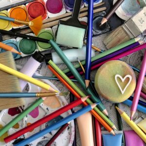A vibrant assortment of art supplies including paints, brushes, and pencils, featuring a heart motif.
