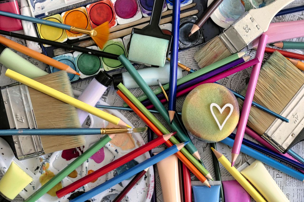 A vibrant assortment of art supplies including paints, brushes, and pencils, featuring a heart motif.